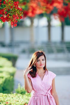 a woman in a pink dress is standing under a tree with red flowers on it