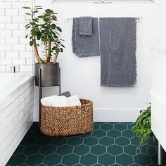 a bathroom with green hexagonal floor tiles and white walls, along with a plant in a basket next to the tub