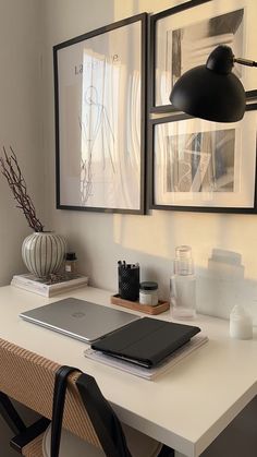 a laptop computer sitting on top of a white desk next to two framed pictures above it