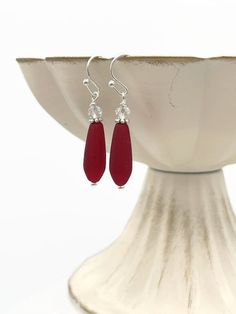 Small, Thin, Frosted Red & Clear Crystal Silver Dangle Drop Earrings. These earrings have a gorgeous cherry or ruby red color on the teardrop bead, accented with a faceted glass clear crystal bead at the top. Semi-transparent when held to the light. The red teardrop bead is made out of recycled glass, it is matte and frosted.  They are only 1-1/2 inches long and 1/4 inches wide, so they are small, dainty, and lightweight! They are perfect if you like earrings that are smaller in size. These are Summer Earrings, Summer Earring, Teardrop Beads, Semi Transparent, Pretty Earrings, Faceted Glass, Bead Earrings, Recycled Glass, Glass Jewelry