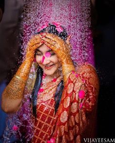 a woman covered in pink and orange powder with her hands on her head, covering her eyes