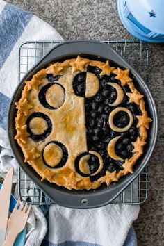 a blueberry pie on a cooling rack next to utensils and a fork