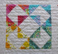 a quilted table topper with colorful designs on it and one block in the middle