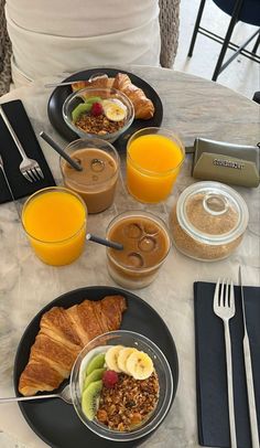 there are many breakfast foods on the table with orange juice and croissants