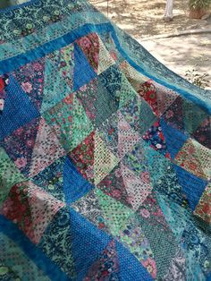 an old quilt is laying on the ground in front of a tree and some bushes