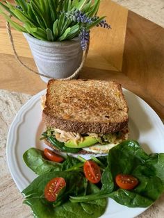 a white plate topped with a cut in half sandwich next to a pile of green leafy vegetables