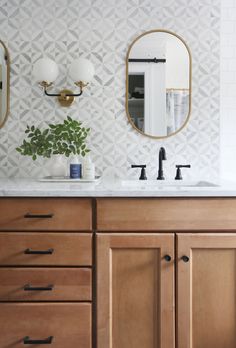 a bathroom vanity with two mirrors above it and a plant on the counter in front of it