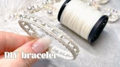 a hand holding a spool of white thread next to a spool of beads