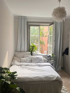 a white bed sitting in a bedroom next to a window with curtains on the windowsill