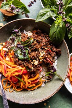 a bowl filled with meat and veggies on top of rice next to greens