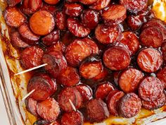 a casserole dish filled with cooked sausages and sauce on a wooden skewer