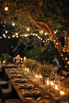 an outdoor dinner table set with candles and place settings in front of a tree at night