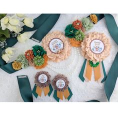 three ribbons and two flower brooches on a white table with flowers in the background