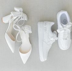 three pairs of white shoes are lined up on the floor, one with a bow