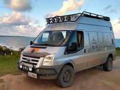 a silver van parked on top of a dirt road next to the ocean and grass