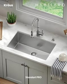 a stainless steel sink in a kitchen with white countertops and gray cabinetry next to a window