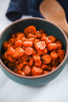 a blue bowl filled with chopped carrots on top of a white tablecloth next to a wooden spoon