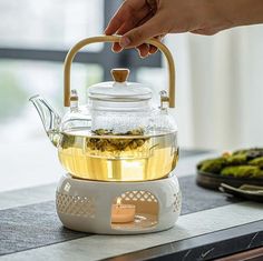 a person holding a tea pot over a kettle filled with green tea on top of a table