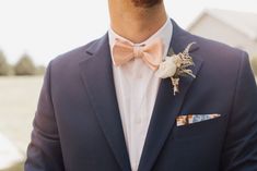 a man in a blue suit with a pink bow tie and boutonniere