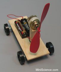 a small toy airplane with batteries attached to it's wings and wheels, on top of a wooden board