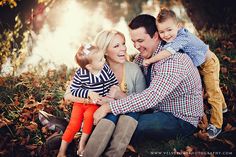 a man, woman and two children sitting on the ground in front of some leaves