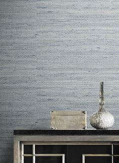 a silver vase sitting on top of a wooden table next to a wallpapered wall