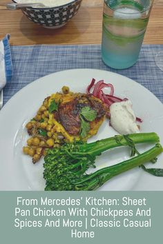 a white plate topped with meat and veggies next to a glass of water