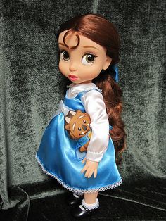 the doll is wearing a blue dress and holding a brown teddy bear in her hand