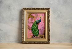 a painting of a peacock in a gold frame on a shelf next to a pink wall