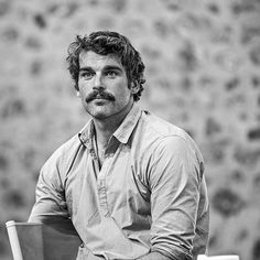 black and white photograph of a man with a mustache sitting on a chair in front of a wall