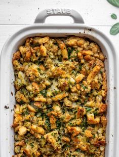 a casserole dish filled with stuffing and vegetables on top of a white table