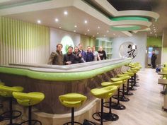 a group of people standing in front of a bar with yellow stools and green seats