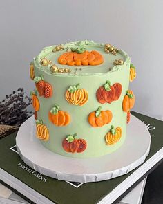 a green cake decorated with pumpkins and leaves on top of a stack of books