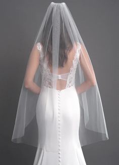 the back of a bride's wedding dress with a veil on her head and shoulder