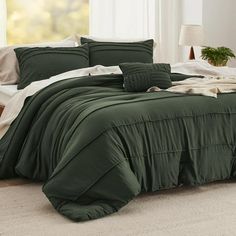 a bed with green comforter and pillows in a room next to a white wall