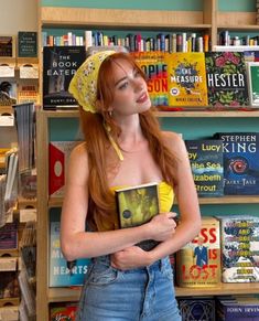 a woman standing in front of a bookshelf holding a book