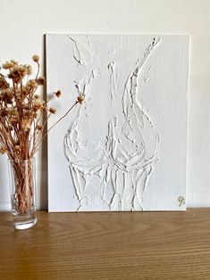 a vase filled with dried flowers sitting on top of a wooden table next to a painting