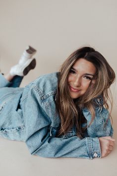 a woman laying on the ground with her legs crossed and smiling at the camera while wearing jeans