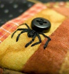 a black button sitting on top of a yellow and red plaid cloth with a spider