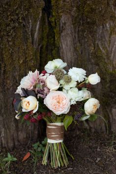 a bouquet of white and pink flowers sitting on the ground next to a tree trunk