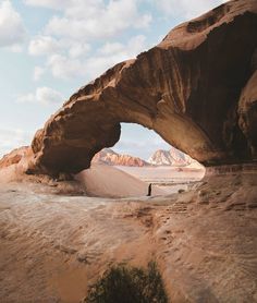 a person standing in the middle of a desert with an arch shaped like a rock