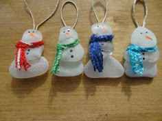 four snowmen are sitting in the shape of small glass ornaments on a wooden table