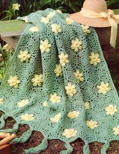 a green crocheted blanket with flowers on it next to a potted plant