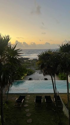 an empty swimming pool with lounge chairs and palm trees in the foreground at sunset