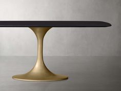 a black and gold dining table with an oval base, on a grey surface in front of a gray wall