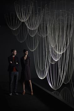 two people standing next to each other in a dark room with white strings hanging from the ceiling