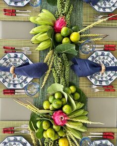 an arrangement of fruits and vegetables on a table with place settings in front of it