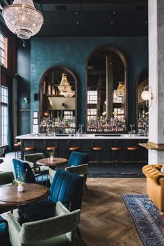 the interior of a restaurant with blue walls and wooden tables, green chairs, and chandeliers