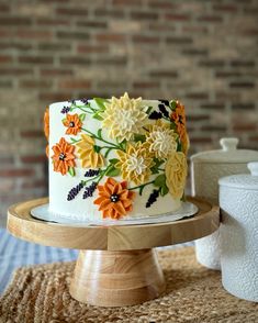 a white cake with orange and yellow flowers on it sitting on a wooden platter