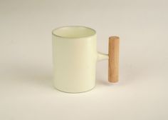 a white cup with a wooden handle on a white surface, next to a small stick